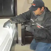 Bed bug inspection technician checking a mattress and bed frame for signs of infestation in Pueblo, CO