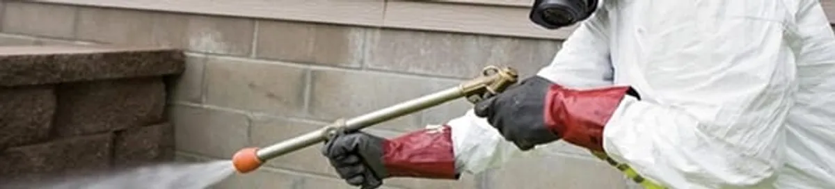 Pest control technician applying exterior insect treatment along a home foundation in Pueblo, CO