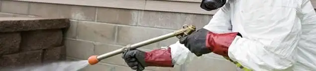 Pest control technician applying exterior insect treatment along a home foundation in Pueblo, CO
