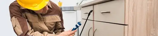 Roach exterminator applying treatment under kitchen cabinets in Pueblo, CO