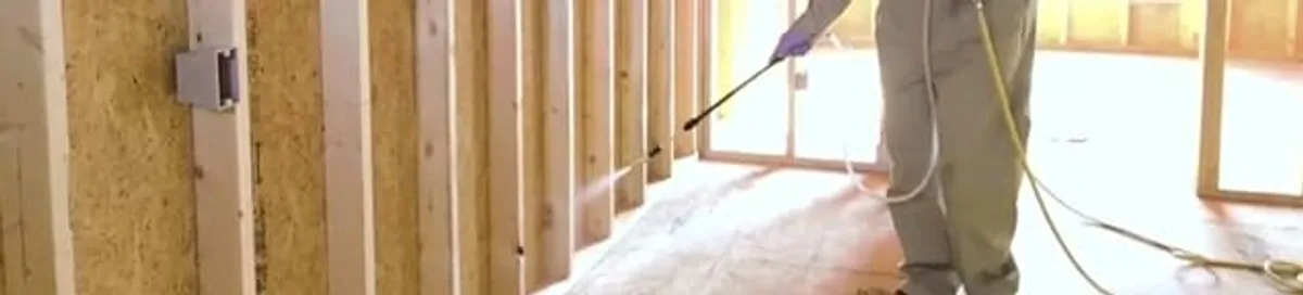 Termite treatment technician applying spray along framing and unfinished walls in Pueblo, CO