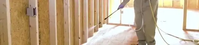 Termite treatment technician applying spray along framing and unfinished walls in Pueblo, CO